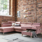 Różowa, rozkładana sofa na tle ceglanej ściany